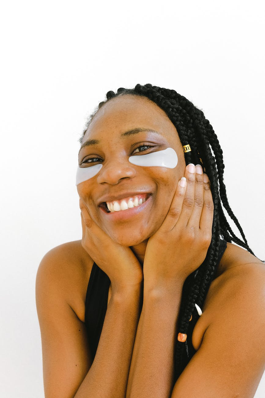 ethnic smiling woman with eye patches and hands on cheeks