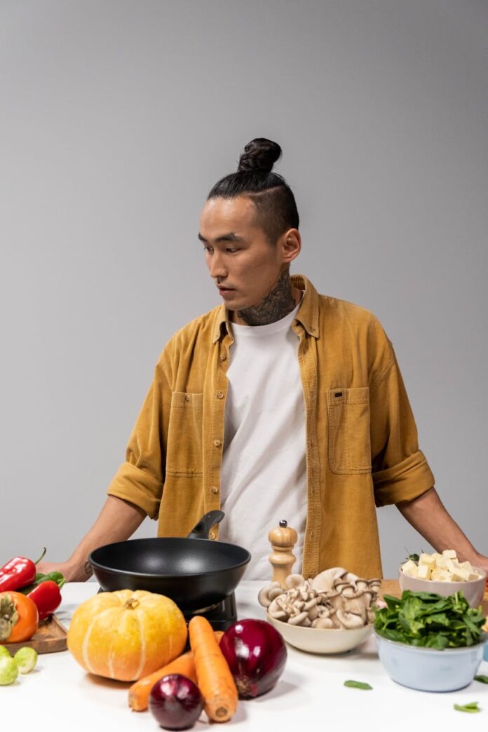 man in mustard yellow corduroy jacket standing near a table with vegetables